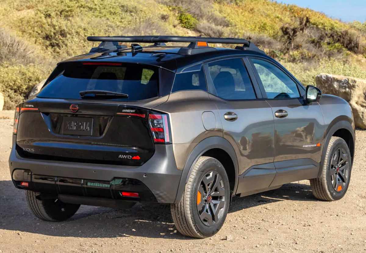 Diseño posterior de la Nissan Kicks Rock Creek AWD en un camino de tierra, exhibiendo su emblema oscuro, la firma lumínica LED y la robusta canastilla portaequipajes superior.