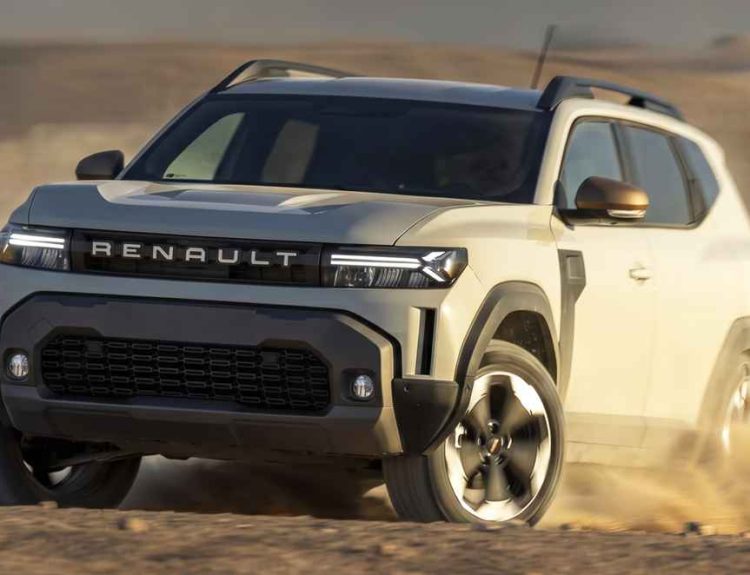 Vista frontal en movimiento de la nueva SUV Renault Duster E-Tech 4x4 color gris claro rodando ágilmente sobre la arena del desierto, destacando su renovada parrilla frontal y faros LED encendidos.