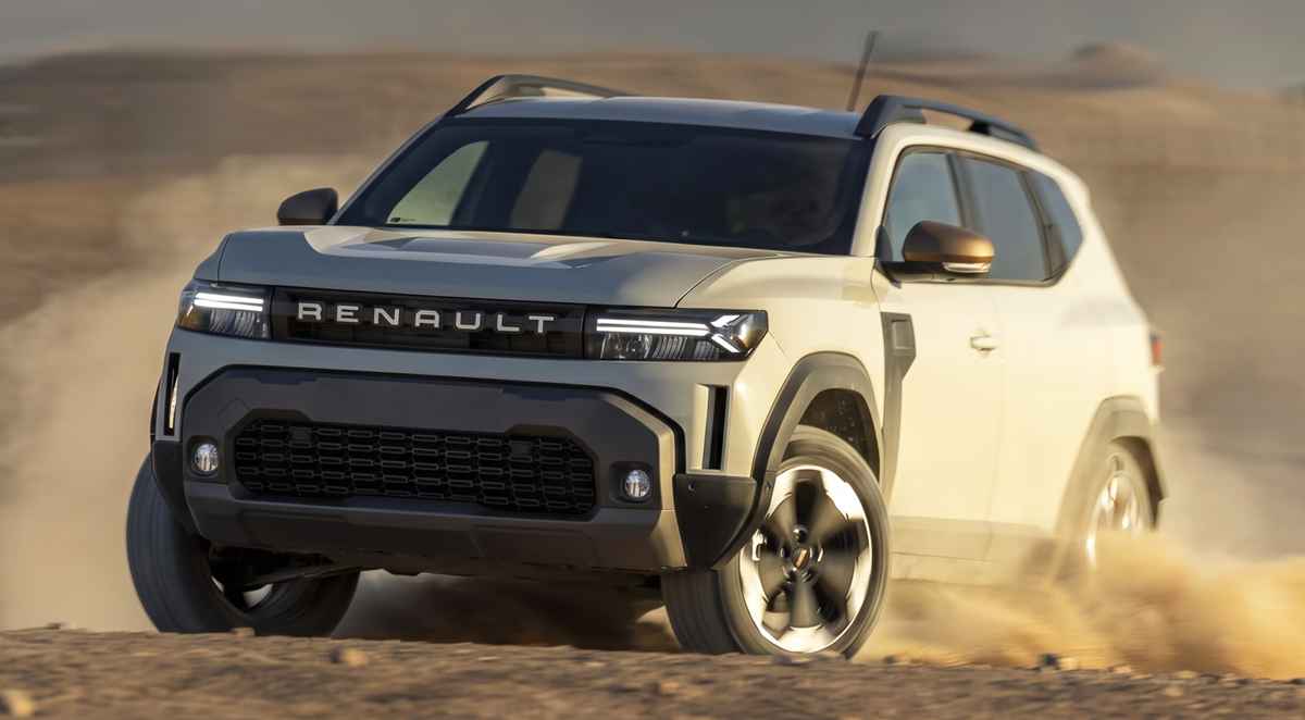 Vista frontal en movimiento de la nueva SUV Renault Duster E-Tech 4x4 color gris claro rodando ágilmente sobre la arena del desierto, destacando su renovada parrilla frontal y faros LED encendidos.