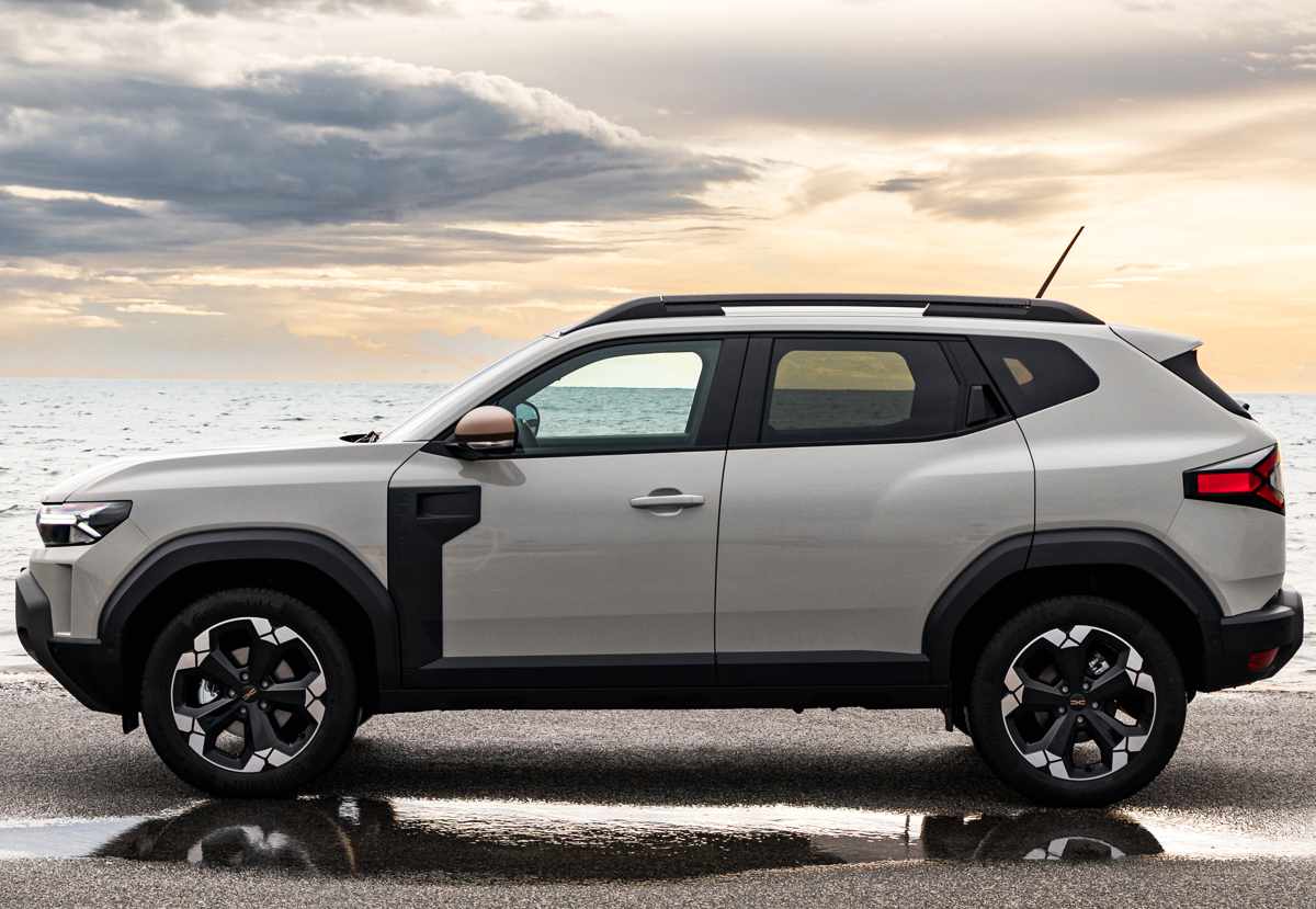 Silueta lateral limpia de la Renault Duster híbrida 4x4 bajo un cielo nublado, destacando sus proporciones rectangulares, barras de techo oscuras y el aplique plástico vertical detrás de las ruedas delanteras.