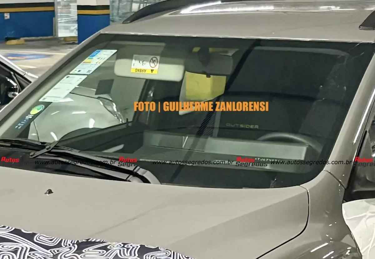 Acercamiento al parabrisas del prototipo del Renault Kwid 2027, dejando entrever desde el exterior el contorno del nuevo panel digital integrado sobre el tablero rediseñado.