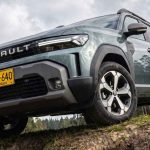 Plano contrapicado de la Renault Duster E-Tech híbrida 4x4 superando un obstáculo en terreno agreste, destacando su amplio despeje al suelo y diseño frontal.