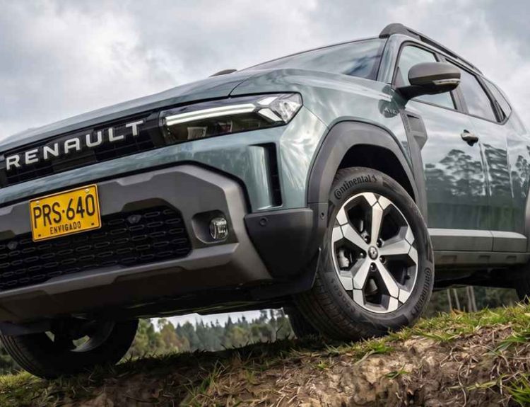 Plano contrapicado de la Renault Duster E-Tech híbrida 4x4 superando un obstáculo en terreno agreste, destacando su amplio despeje al suelo y diseño frontal.