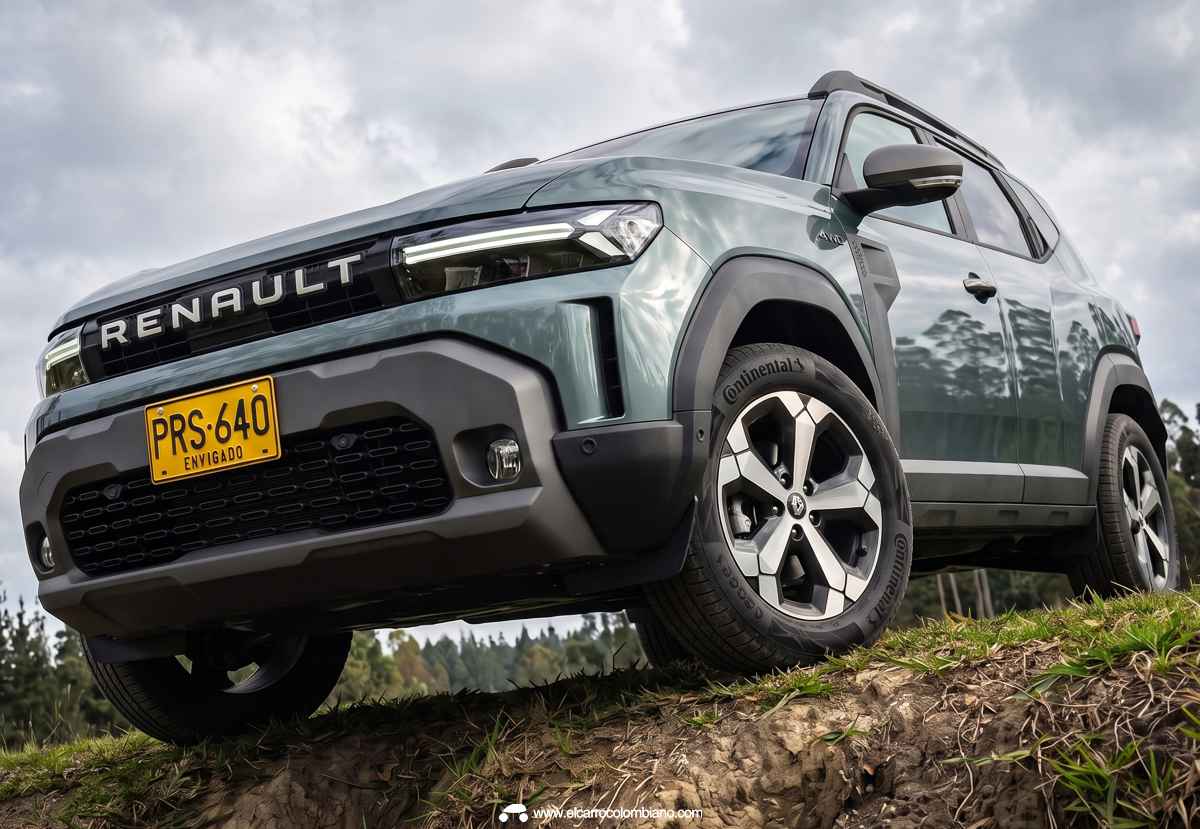 Plano contrapicado de la Renault Duster E-Tech híbrida 4x4 superando un obstáculo en terreno agreste, destacando su amplio despeje al suelo y diseño frontal.