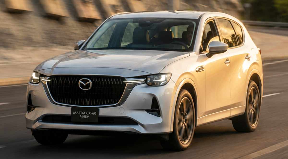 Plano frontal en movimiento de la Mazda CX-60 Híbrida Enchufable color plata, transitando por carretera al atardecer, destacando su imponente diseño Kodo.
