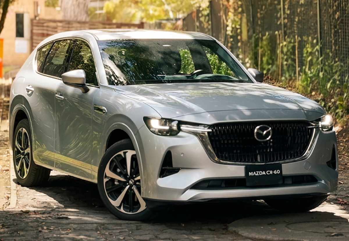 Vista frontal de tres cuartos de la Mazda CX-60 Híbrida Enchufable plateada, estacionada en una calle adoquinada, resaltando su elegante parrilla y faros LED.