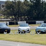 Plano general de los tres carros eléctricos Arcfox T1, S5 y T5 estacionados sobre una pista de pruebas, destacando las letras gigantes de la marca en primer plano.