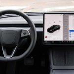 Plano general del interior de un Tesla sin pasajeros, enfocándose en el volante y la pantalla central táctil encendida desde donde se gestiona la Conectividad Premium.