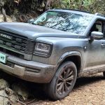 Plano frontal de tres cuartos de la SUV GWM Haval H7 Full Hybrid color gris oscuro superando un obstáculo rocoso en un camino de tierra, destacando su robusta parrilla y capacidades 4WD.
