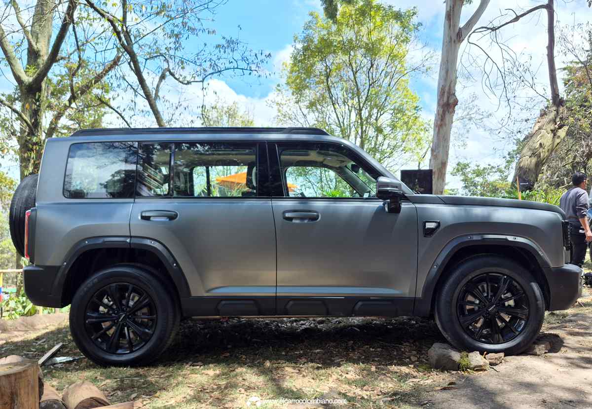 Plano lateral completo de la GWM Haval H7 Full Hybrid color gris mate estacionada sobre un terreno destapado, exhibiendo su altura libre al suelo de 22,1 cm, molduras plásticas y rines negros de 19 pulgadas.