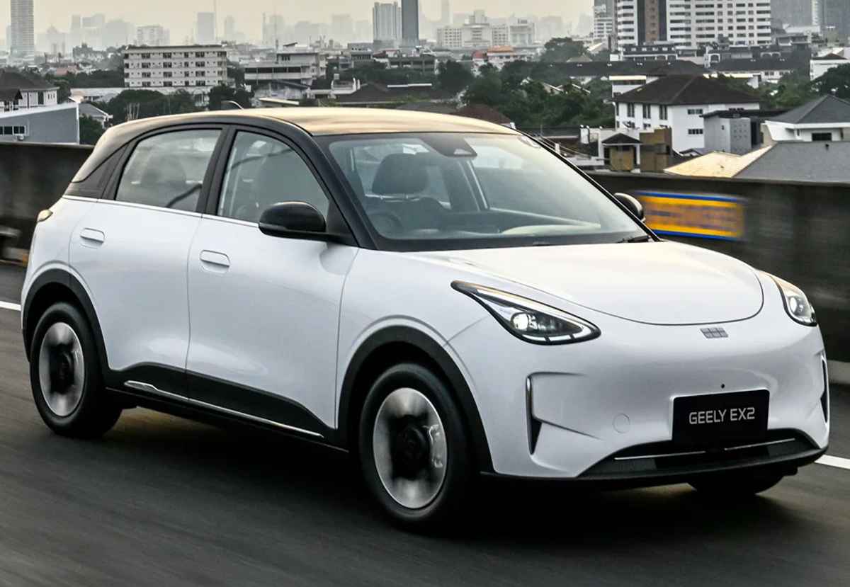 Plano frontal de tres cuartos del hatchback eléctrico Geely EX2 color blanco rodando dinámicamente por una autopista urbana, mostrando su silueta aerodinámica y techo panorámico oscuro.
