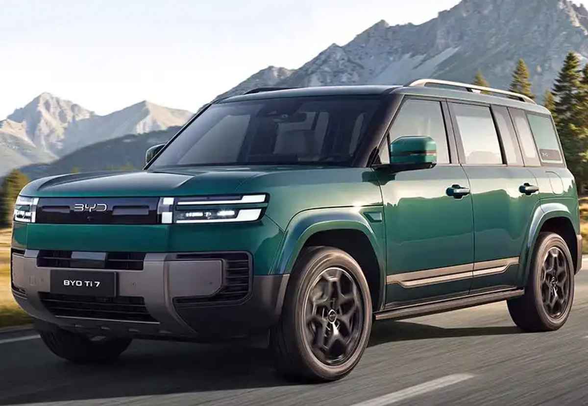 Plano frontal de tres cuartos de la camioneta todoterreno BYD Ti7 color verde circulando por una carretera asfaltada con montañas al fondo, exhibiendo su diseño robusto y rines deportivos.