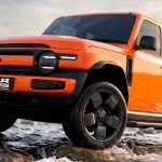 Plano frontal de tres cuartos del campero eléctrico iCAUR V23 color naranja cruzando un arroyo rocoso, destacando sus faros redondos retro y excelentes capacidades off-road.