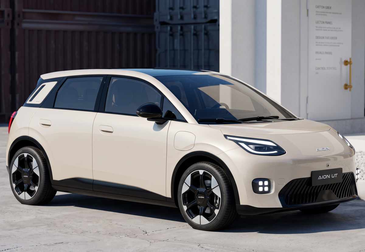 Plano frontal de tres cuartos del GAC Aion UT color beige estacionado frente a una estructura industrial blanca, exhibiendo su techo flotante oscuro y diseño aerodinámico en forma de cuña.