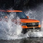 Plano frontal de tres cuartos de la Jetour G700 naranja cruzando un río a velocidad, demostrando su capacidad de vadeo de hasta 90 centímetros y su tracción 4x4.