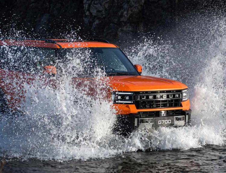 Plano frontal de tres cuartos de la Jetour G700 naranja cruzando un río a velocidad, demostrando su capacidad de vadeo de hasta 90 centímetros y su tracción 4x4.
