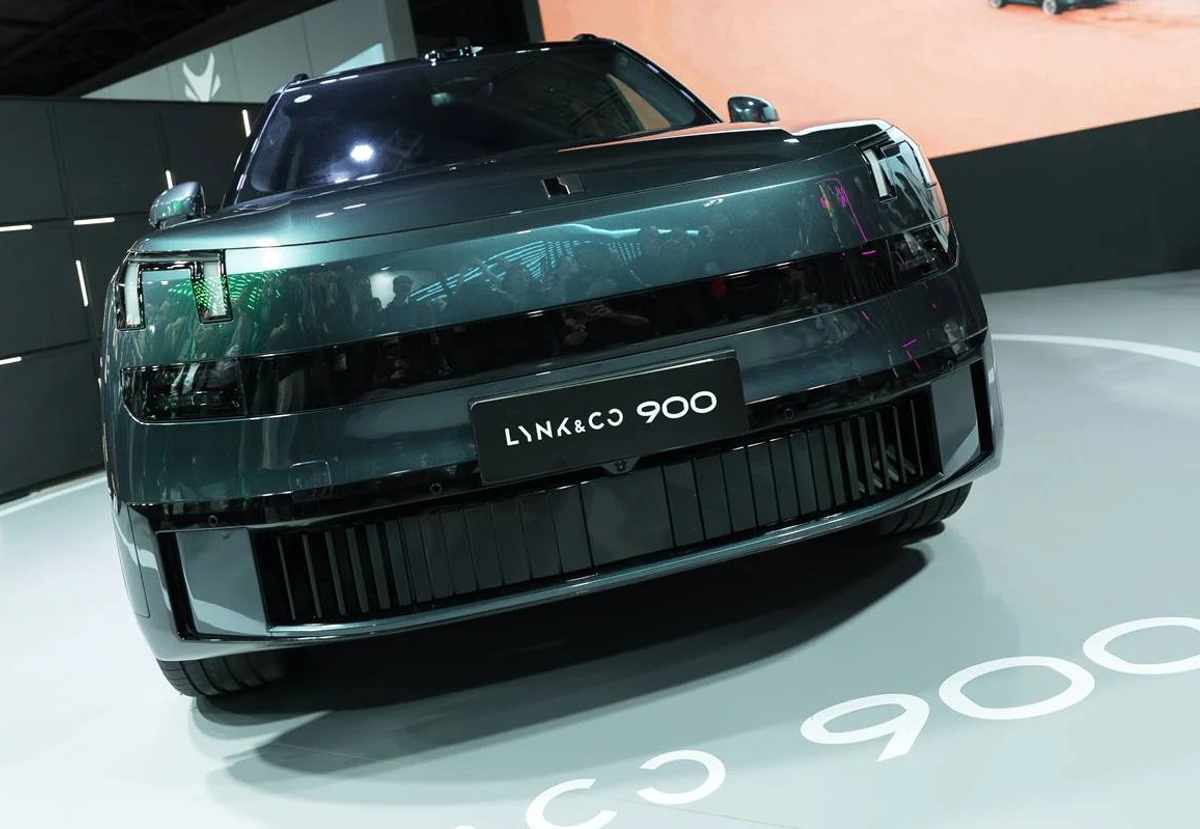 Plano frontal directo de la imponente camioneta Lynk & Co 900 oscura sobre una plataforma, exhibiendo su parrilla inferior con franjas verticales y su distintiva firma lumínica LED.