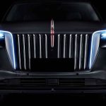 Plano detalle frontal de un vehículo Hongqi E-HS9 sobre fondo oscuro, destacando su imponente parrilla cromada de franjas verticales y la emblemática línea roja iluminada central.