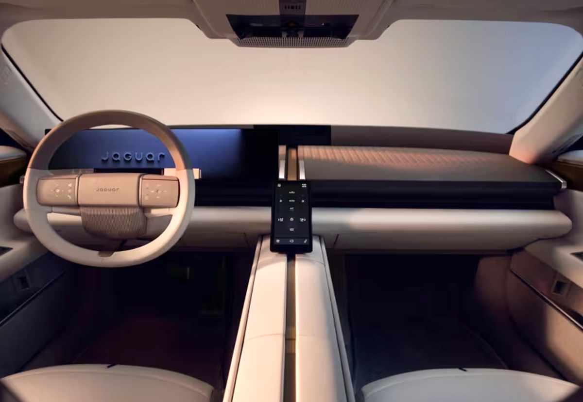 Plano general del tablero interior del Jaguar Type 01, mostrando un diseño minimalista en tonos claros con acabados inspirados en latón, volante de formas cuadradas y la gran consola central con pantalla de controles.