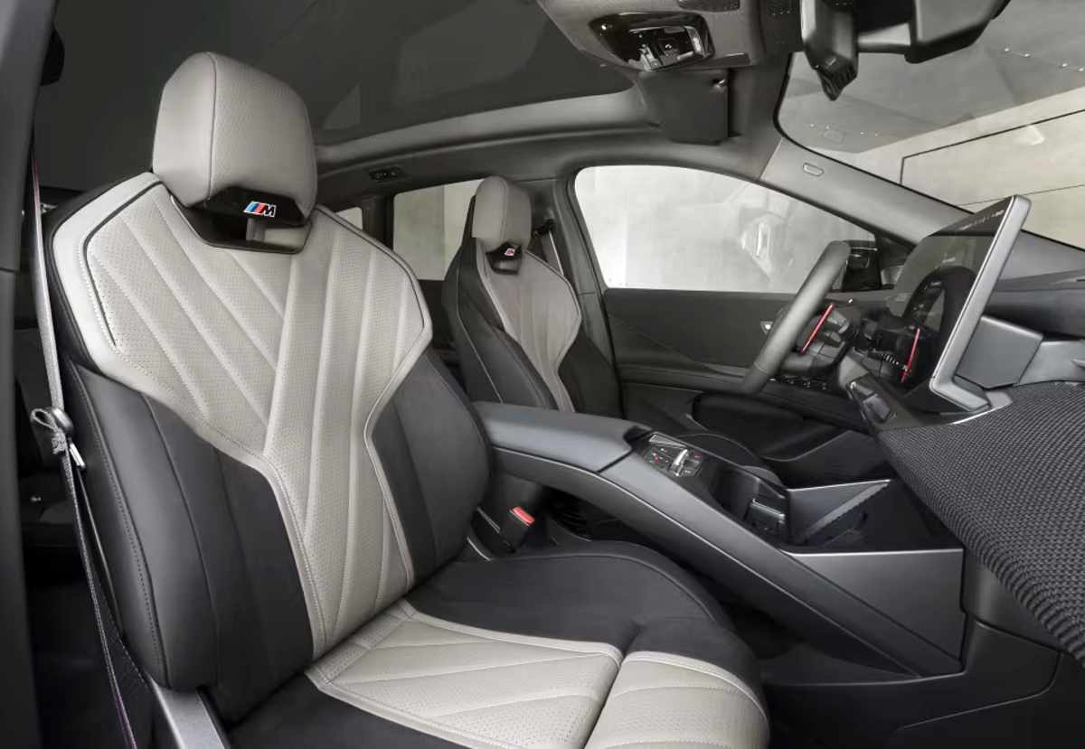 Vista interior de la cabina de la BMW iX3 M60 xDrive, detallando los asientos deportivos M Sport con tapicería bitono clara y oscura, detalles de costuras y los emblemas M retroiluminados.