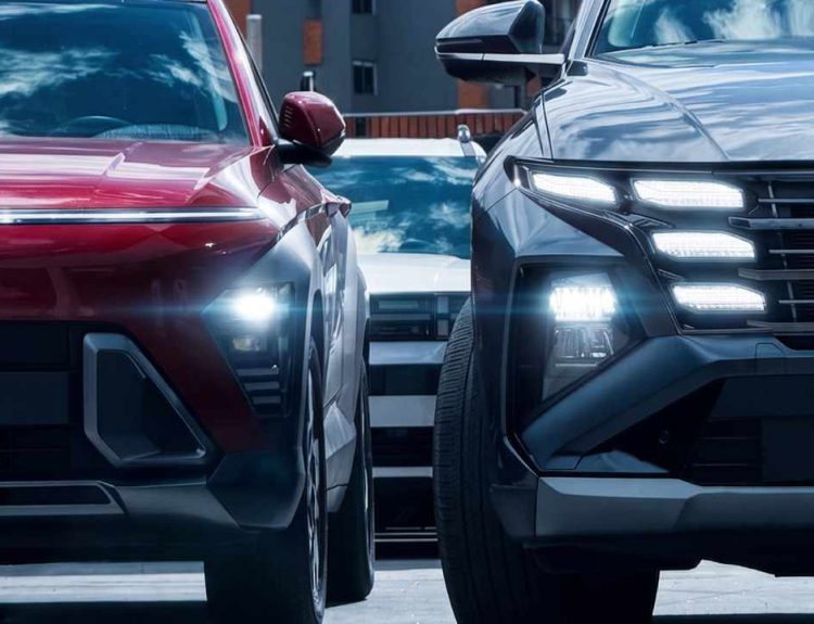 Plano frontal de detalle de dos camionetas híbridas estacionadas una junto a la otra, destacando a la izquierda el diseño moderno de la Hyundai Kona roja y a la derecha la parrilla con luces LED de la Hyundai Tucson gris.