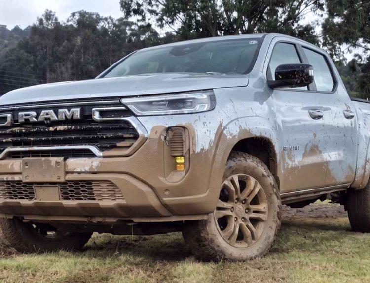 Plano frontal de tres cuartos de la pick-up RAM Dakota plateada con la carrocería cubierta de barro en un entorno campestre, destacando su vocación todoterreno y robusta parrilla frontal.