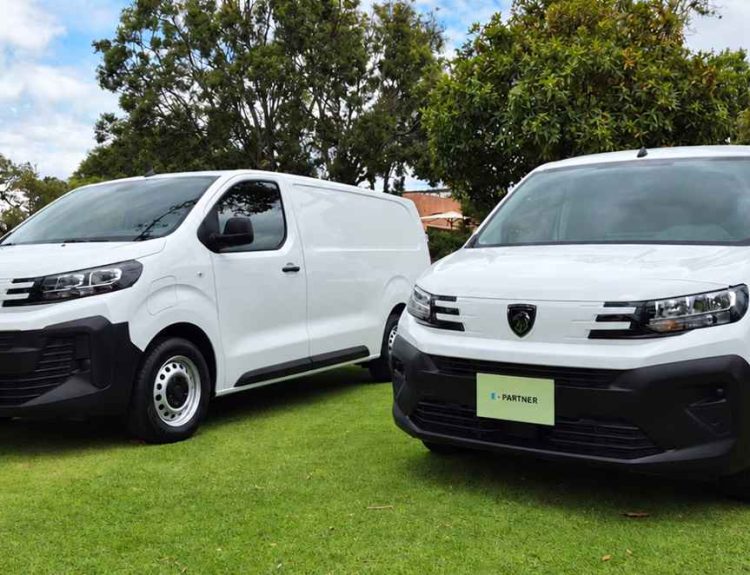 Plano frontal de tres cuartos de las furgonetas eléctricas Peugeot e-Expert y e-Partner de color blanco estacionadas juntas sobre el césped, destacando sus robustos parachoques negros.