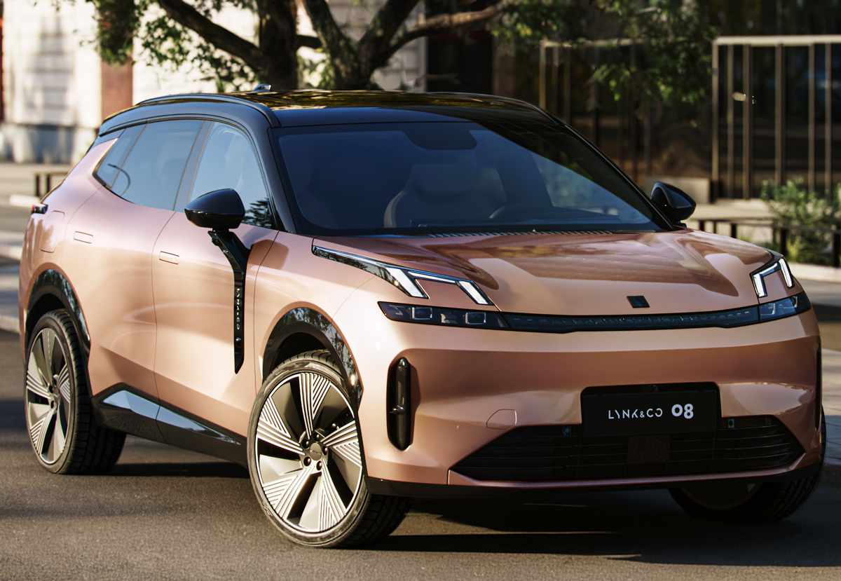 Plano frontal de tres cuartos de la SUV Lynk & Co 08 en tono cobrizo con techo negro estacionada sobre el asfalto en un entorno urbano iluminado por el sol, destacando sus peculiares luces diurnas sobre el capó y rines aerodinámicos.