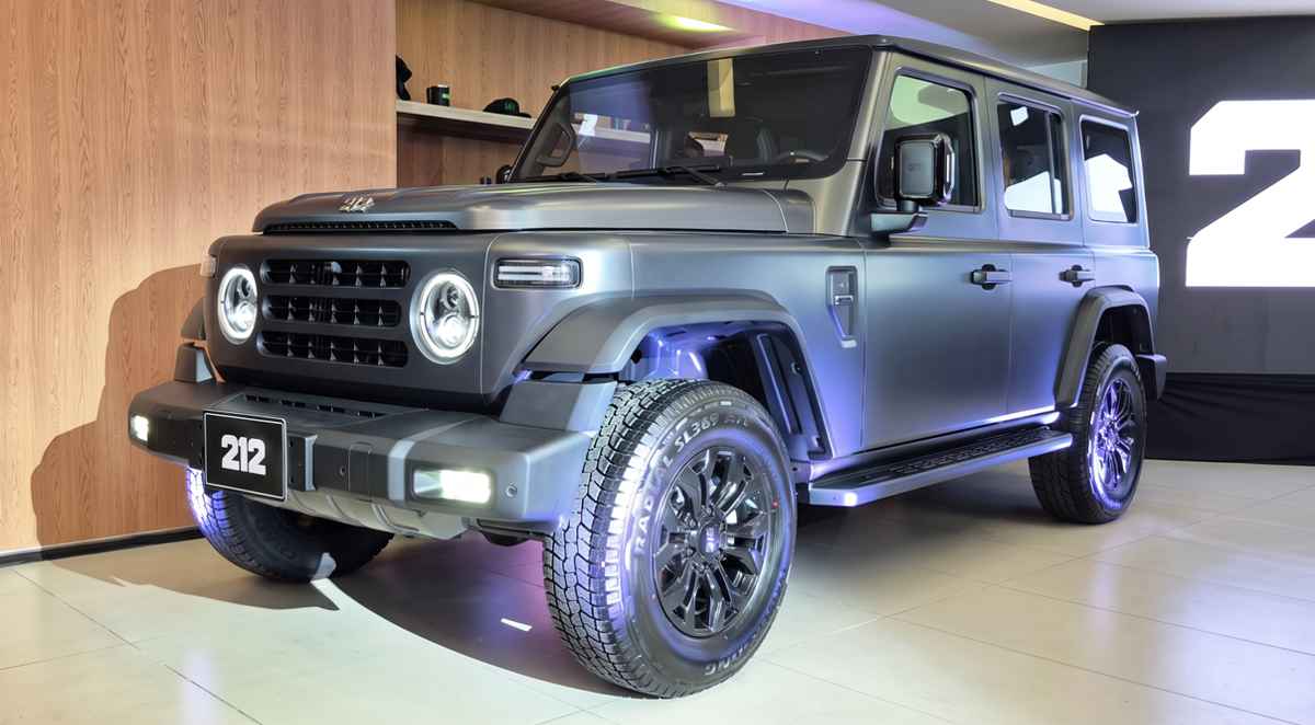 Plano frontal de tres cuartos del campero 212 T01 color gris mate exhibido en salón de lanzamiento en Colombia, destacando su carrocería cuadrada retro, faros LED redondos y llantas todoterreno.