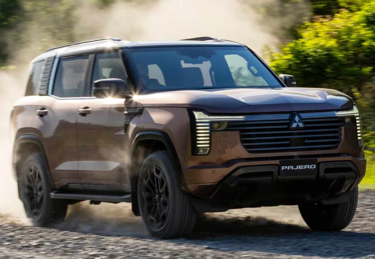 Plano frontal de tres cuartos de la nueva Mitsubishi Montero café con placa Pajero avanzando a velocidad sobre una trocha destapada y levantando polvo, demostrando sus capacidades todoterreno 4x4.
