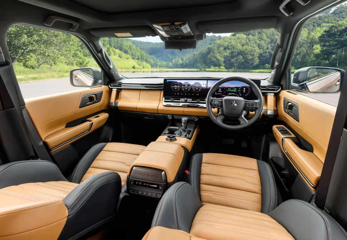 Plano general del interior de la nueva Mitsubishi Montero con tapicería en cuero color camel y negro, destacando sus asientos deslizables y el tablero con dos pantallas de 14,3 pulgadas que muestran los clásicos relojes de inclinación y altitud.