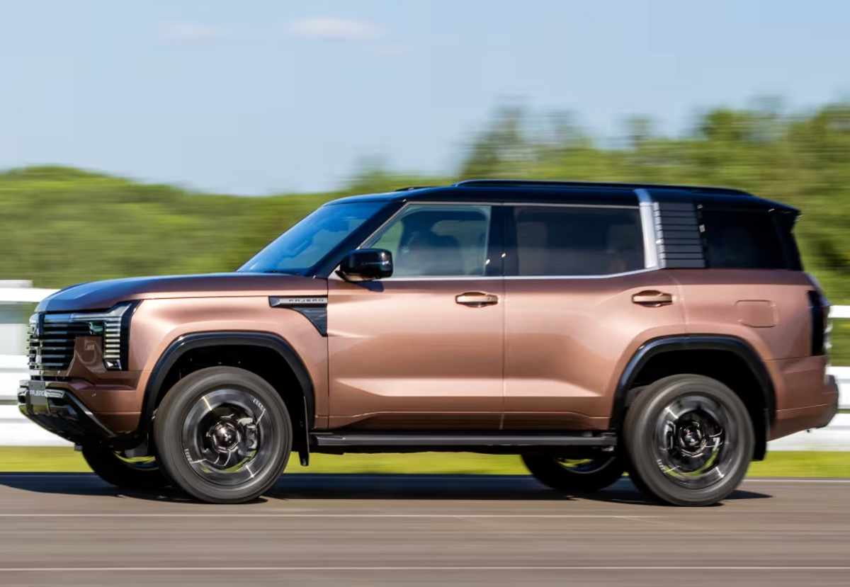Plano lateral completo de la nueva Mitsubishi Montero 2027 café con techo negro en movimiento, evidenciando su carrocería cuadrada de 4,92 metros de largo, 23 centímetros de altura al suelo y rines negros.