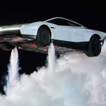Plano de tres cuartos lateral del nuevo deportivo eléctrico Tesla Roadster blanco levitando a gran altura durante una demostración nocturna, impulsado por tres potentes y densos chorros de gas de sus cohetes de SpaceX que generan una enorme nube de humo blanco en el suelo, con el horizonte oscuro de fondo.