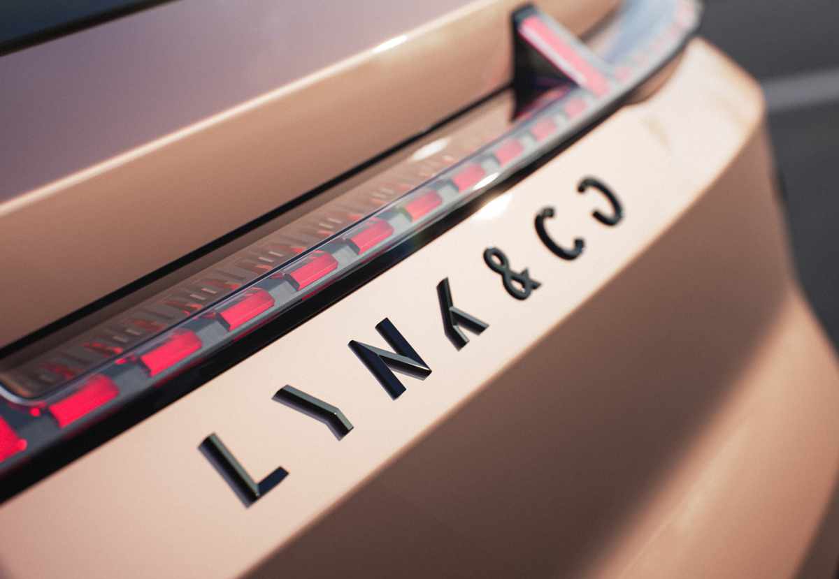 Plano detalle de la parte trasera de un vehículo Lynk & Co color cobre, enfocando las letras negras del emblema de la marca bajo la franja de luces LED rojas con diseño de bloques tridimensionales.